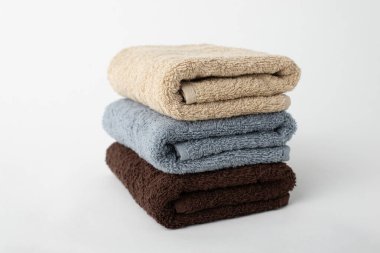 Beyaz arka planda izole edilmiş üç adet pamuklu havlu yığını. Suyu silmek ve emmek için bej, gri ve kahverengi terry havlular..
