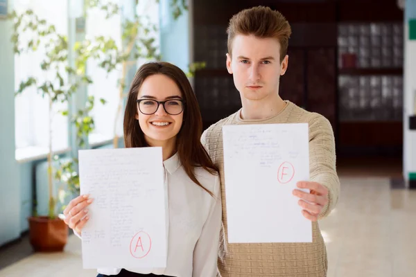 Male and female students showing results of final examination to the camera. Concept of differenciation, differet test result