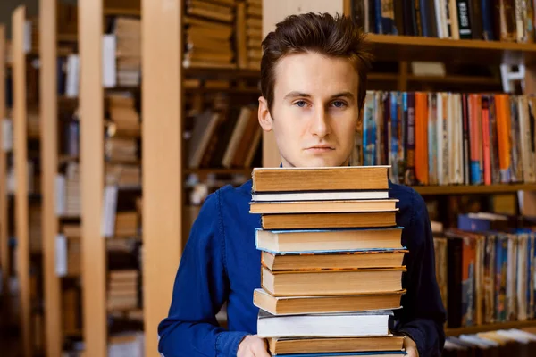 Άνδρας Μαθητής Στέκεται Ένα Σωρό Βιβλία Στη Βιβλιοθήκη Και Κοιτάζει — Φωτογραφία Αρχείου