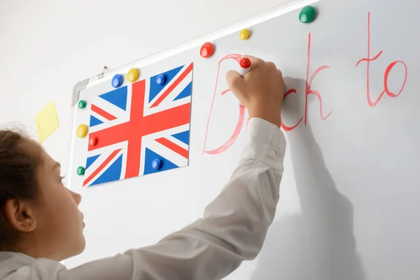 穿着白衬衫的小女孩在白板上写着红字 英国国旗和船上五彩斑斓的磁铁 回到学校的概念 — 图库照片