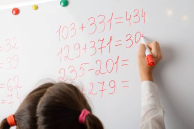 Matematik dersi sırasında beyaz tahtada matematik denklemleri hesaplayan genç bir ilkokul öğrencisi. Eğitim, matematik konsepti.