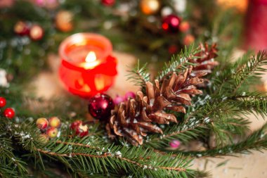 Noel çelengi, koni, yapay böğürtlen ve kar ile süslenmiş. Ortasında yanan kırmızı mum, sıcak atmosfer..