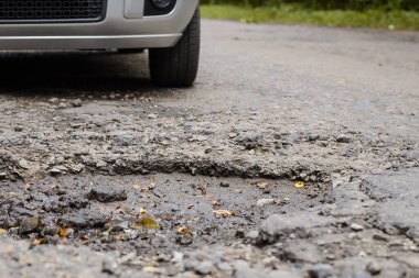 Asfalt yüzeyindeki bir yol boşluğunun yakın çekimi ve yaklaşan bir araba. Kötü yol.