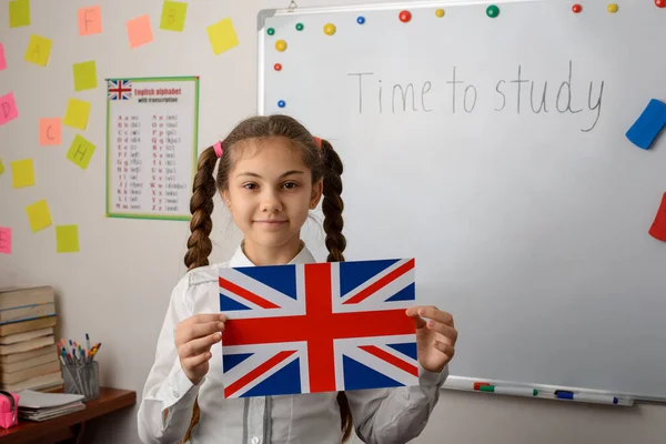 Female student of language courses with flag of United Kingdom in classroom. Smiling schoolgirl represents concept of language learning with fun.