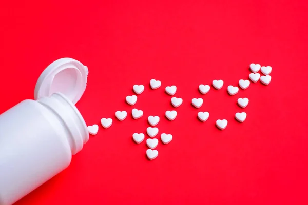 Heart shaped white pills make signs of man and woman on red background. White open medicine bottle near tablets.