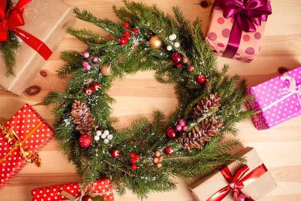 Green handmade fir-tree wreath on wooden table. Colorful christmas presents, new year mood.