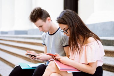 Konsantre genç erkek ve kız akıllı telefonlarına bakıp derslerden önce malzeme arıyorlar. Dışarıdaki insanlar, öğrenci hayatı, modern teknolojiler..