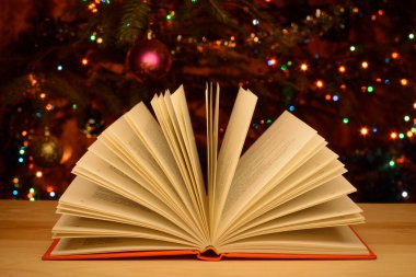 Arka planda süslenmiş Noel ağacı olan açık bir kitap. Noel okumaları, şenlikli sakin rahat atmosfer