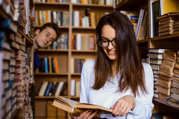 図書館で本を読んでいる女性学生と 彼女をスパイすることを愛する別の男性学生 面白い教育 教育中の愛 — ストック写真