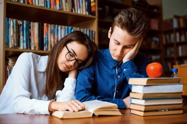 Kütüphanede sıkılmış iki öğrenci. Erkek ve bayan öğrenciler son zamanlarda okudukları pek çok kitap yüzünden final sınavlarına hazırlanmaktan bıkıp usandılar.