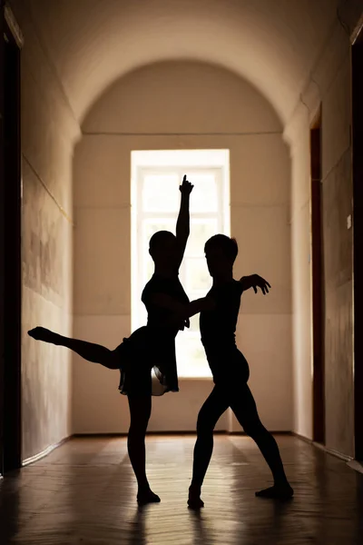 Silhouettes of two professional dancers performing classical dance in the corridor of an old theatre. Beautiful shot of elegant dancers