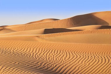 Sıcak turuncu kum tepeleri ve mavi gökyüzü olan çöl manzarası.