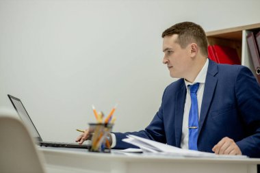 Belgelerle çalışan genç işadamı dosyalara bakıyor, büro masasında oturuyor.