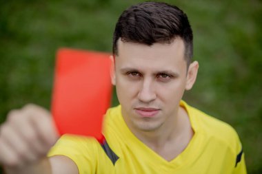 Hakem, hoşnutsuz bir futbol oyuncusu ya da futbolcuya kırmızı kart gösteriyor. Spor anlayışı, kural ihlali, tartışmalı konular, engellerin aşılması