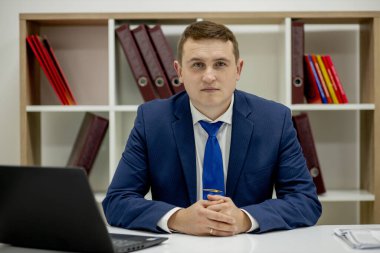 Tipik çalışma günü. Ofisinde oturan ve dizüstü bilgisayarına bakan kendinden emin genç bir iş adamının fotoğrafını çek..