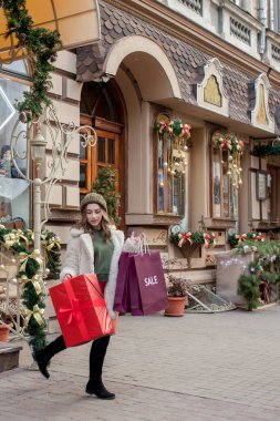 Mutlu kadın elinde hediye kutusuyla mağazadan çıkarken gülümsüyor. Güzel mutlu kız Noel hediyeleriyle poz veriyor. Yeni yıl hazırlığı.