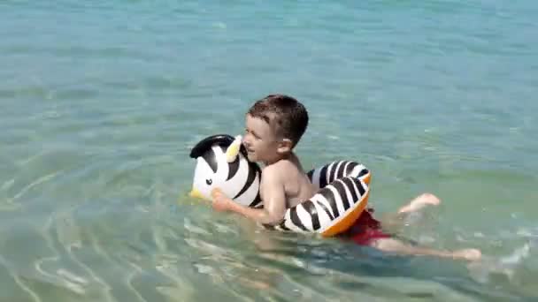 Kind schwimmt im Meer mit einem aufblasbaren Kreis. Sommerurlaub aktive Freizeit.Glückliche Kindheit. — Stockvideo