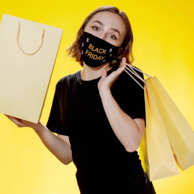 Kara Cuma indirimi. Elinde Kara Cuma alışveriş torbaları olan maskeli bir kadın. Salgın sırasında satış.