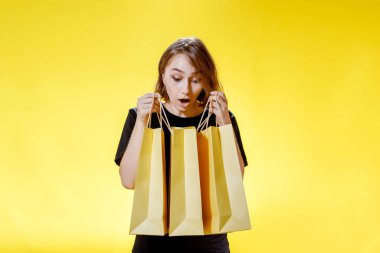 Sarı arka planda paketleri olan neşeli bir kadın, alışveriş gezisi. Stüdyo portresi. Kara Cuma indirimi.