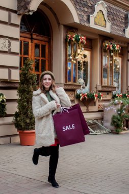 Mutlu kız, dükkanlarda satıştan sembollerle dolu kağıt torbaları tutuyor. Noel 'de, şehrin her yerinde satışları var. Alışveriş kavramı, tatiller, mutluluk, Noel satışları