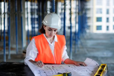 Mimar ya da mühendis, bina inşaatı projesini bina içinde ayrıntılı bir planla inceliyor. Kadın inşaat mühendisleri veya mimarlar çalışan insanlar.