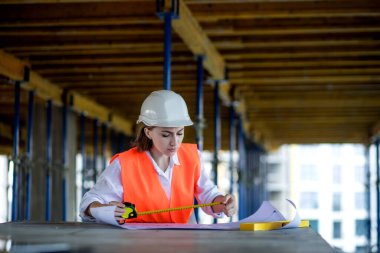 Mimar ya da mühendis, bina inşaatı projesini bina içinde ayrıntılı bir planla inceliyor. Kadın inşaat mühendisleri veya mimarlar çalışan insanlar.