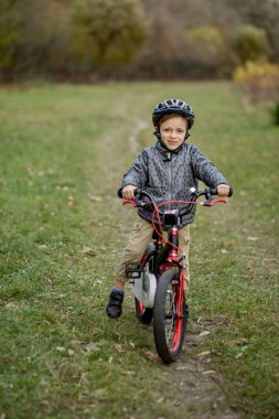 Kasklı bir çocuk parkta bisiklet sürüyor..