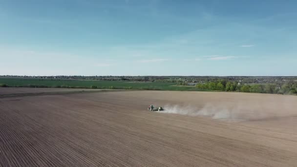 Aerial view of tractor with harrow system plowing ground on cultivated farm field, pillar of dust trails behind, preparing soil for planting new crop, agriculture concept, top view — Stock Video