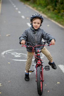 Kasklı küçük bir çocuk parktaki bisiklet yolunda bisiklet sürüyor..