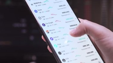 Kyiv, Ukrayna 24 Kasım 2021: Tüccar cep telefonu ekranında Bitcoin ve diğer kripto carrency grafiğini kontrol ediyor. Telefon uygulaması kullanarak mali analiz. Piyasa ticareti karı.