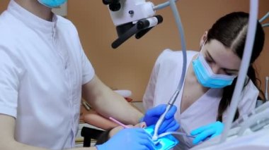 Bir dişçi, bir kadının dişlerini kabartma barajı kullanarak tedavi eder. Diş ekipmanları.