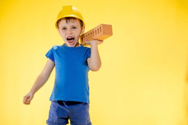 İnşaat kasklı çocuk elinde sarı arka planda bir tuğla tutuyor..