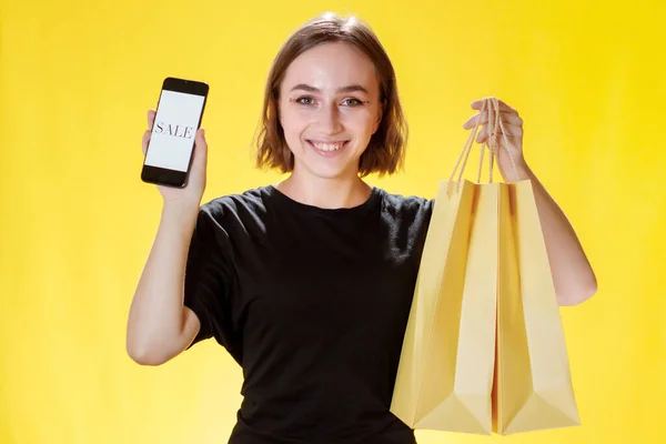 Kaukázusi Fiatal Mosolyog Tartja Mobiltelefon Bevásárló Csomag Nézi Telefon Képernyőjén — Stock Fotó