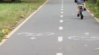 Kasklı küçük bir çocuk parktaki bisiklet yolunda bisiklet sürüyor..