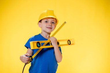 İnşaat seviyesi olan miğferli anaokulu öğrencisi inşaatçıyı oynuyor..