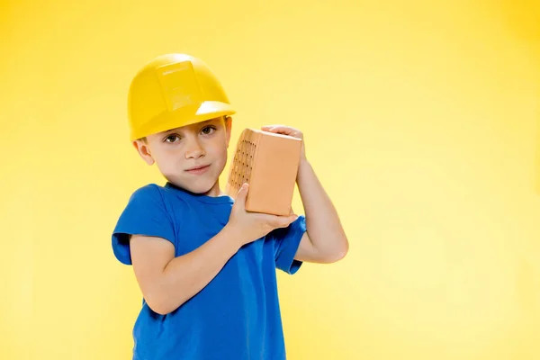 Jongen Een Bouwhelm Houdt Een Baksteen Zijn Handen Gele Achtergrond — Stockfoto