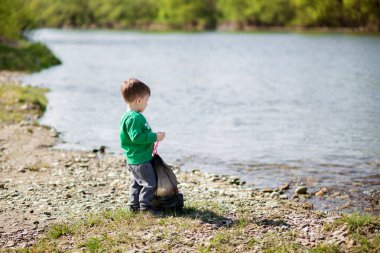 Küçük çocuk çöpleri ve plajda plastik şişeleri toplayıp çöpe atıyor. Çevre kavramını kaydet.