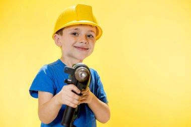 Elinde matkap tutan, mavi gömlekli, gülümseyen çocuk..