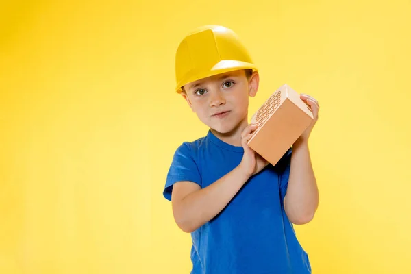 Chlapec Stavební Helmě Drží Cihlu Svých Rukou Žlutém Pozadí — Stock fotografie