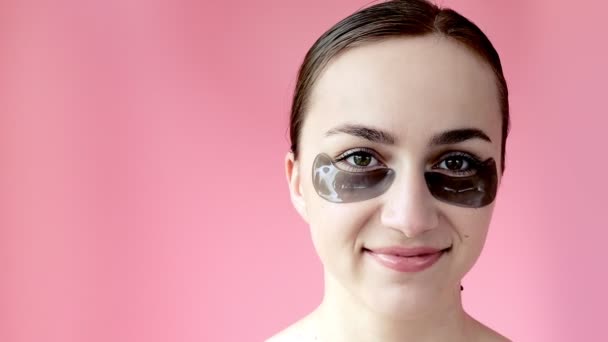 女性は鏡の反対側に座って笑って 彼女の目の下に黒いパッチを使用します 健康的なライフスタイル — ストック動画