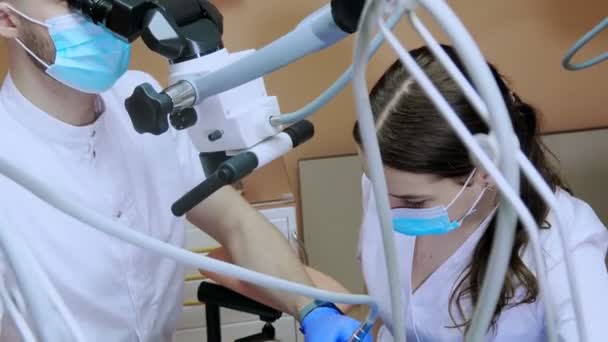 Dentista Con Asistente Bajo Microscopio Trata Los Dientes Del Paciente — Vídeos de Stock