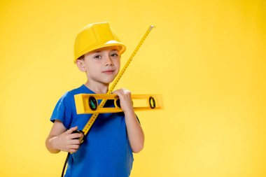 İnşaat seviyesi olan miğferli anaokulu öğrencisi inşaatçıyı oynuyor..