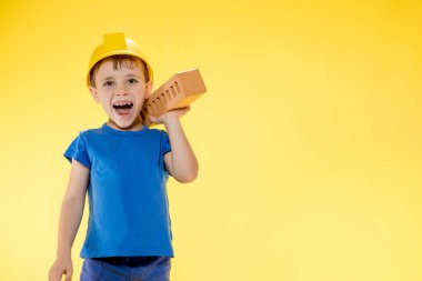 İnşaat kasklı çocuk elinde sarı arka planda bir tuğla tutuyor..