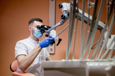 Erkek bir dişçi mikroskoba bakar. Yeni teknolojiler kullanan modern dişçilik.