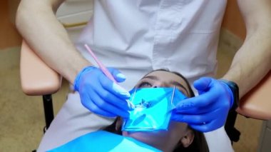 Bir dişçi, bir kadının dişlerini kabartma barajı kullanarak tedavi eder. Diş ekipmanları.