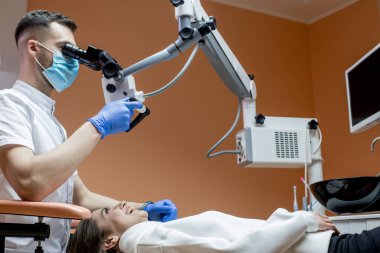 Dişçi mikroskopla hastanın dişlerine bakıyor. Modern ilerici dişçilik.