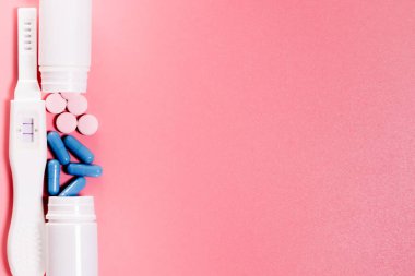 İki şeritli hamilelik testi, pembe ve mavi haplar. Pastel pembe arka plan. Pozitif sonuç. Hamile bir kadının tedavisi için. Boşluğu kopyala.