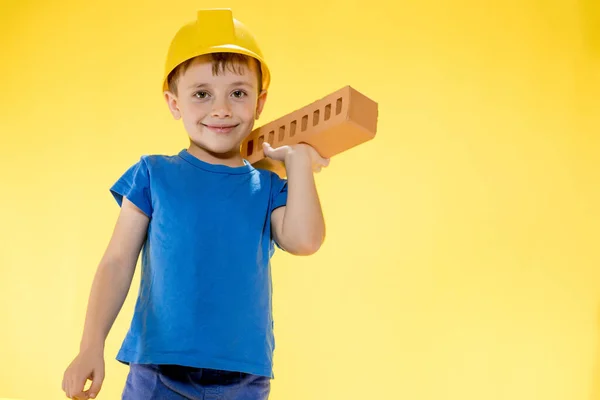 Niño Casco Construcción Sostiene Ladrillo Sus Manos Sobre Fondo Amarillo — Foto de Stock