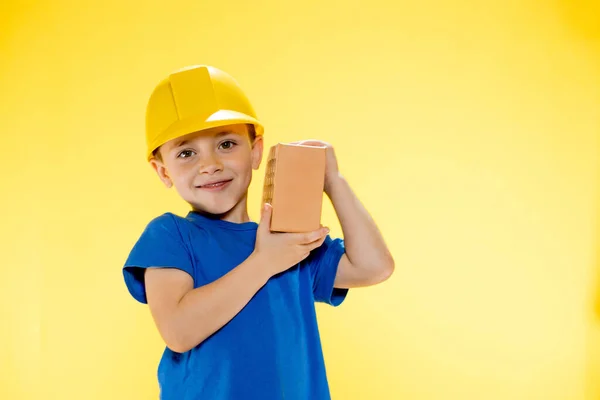 Menino Capacete Construção Segura Tijolo Suas Mãos Fundo Amarelo — Fotografia de Stock