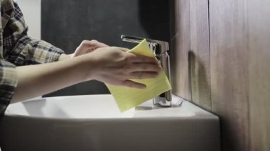 Bir kadının eli bir bez parçası tutar ve banyodaki musluğu siler. Banyoyu temizliyorum.